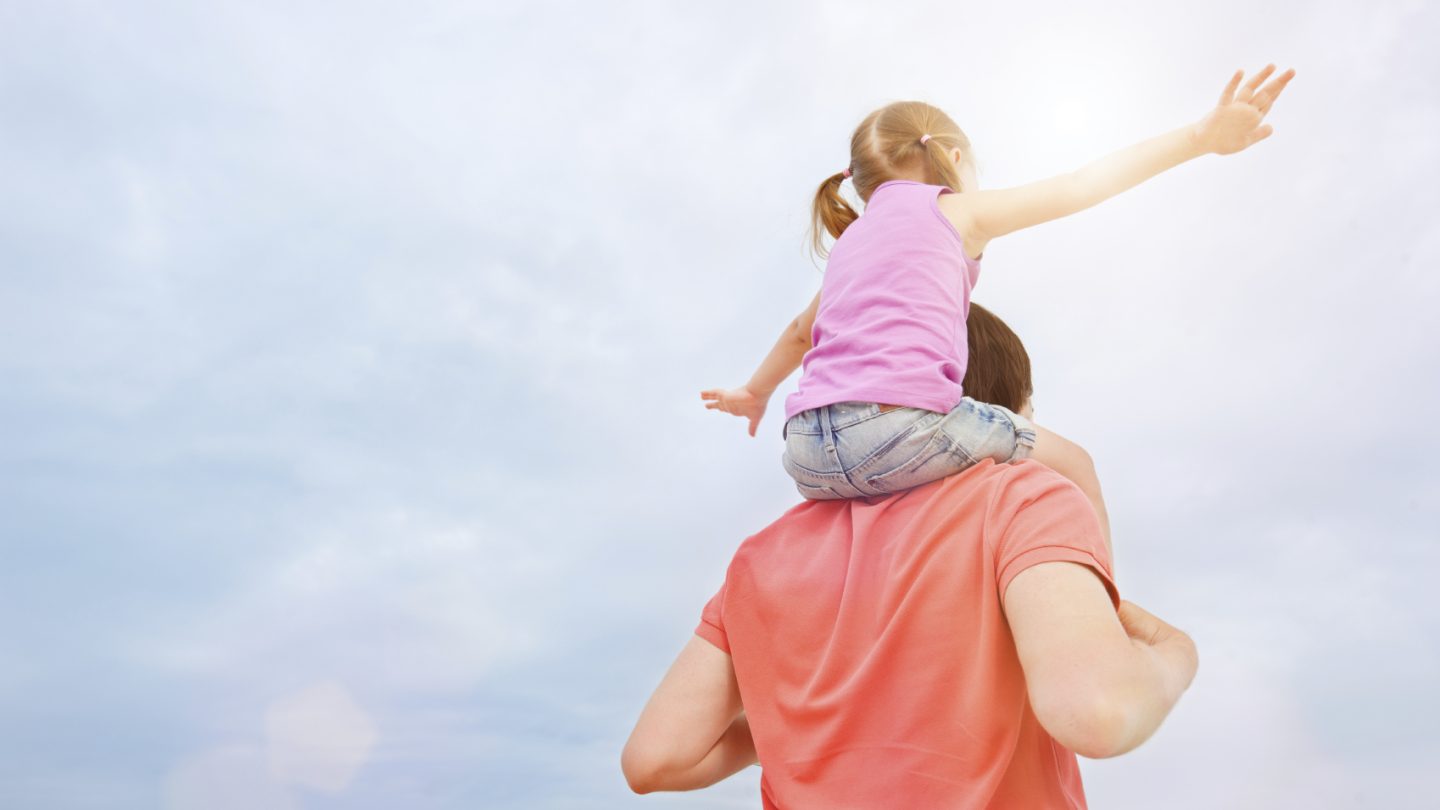 Back view of father carrying his little daughter on shoulders