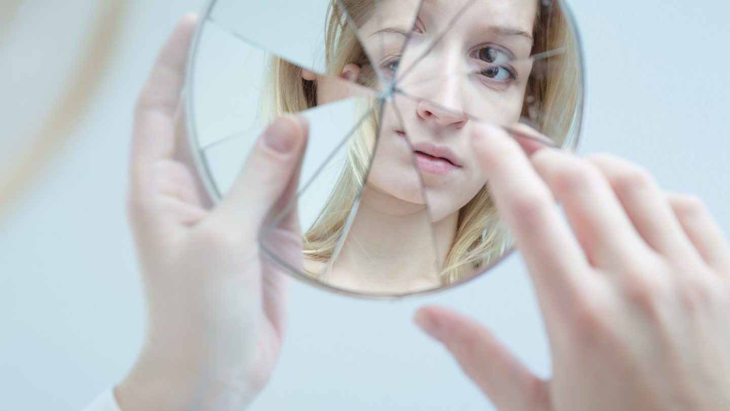 Insecure pretty young woman holding broken mirror
